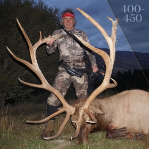 A man posing next to a red stag with horns almost as tall as him.