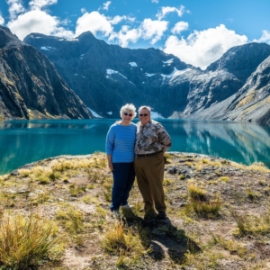 A happy couple smiling and posing in front of a lake and mountains during their New Zealand adventure.