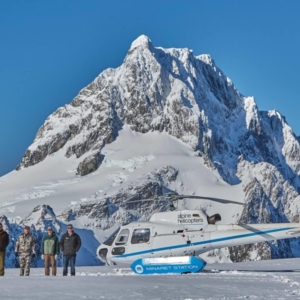 Five men posing next to a helicopter in front of a snow-covered mountain before their New Zealand hunt.