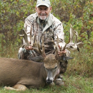 A man smiling and holding the large whitetail buck he harvested during his Wisconsin hunt.